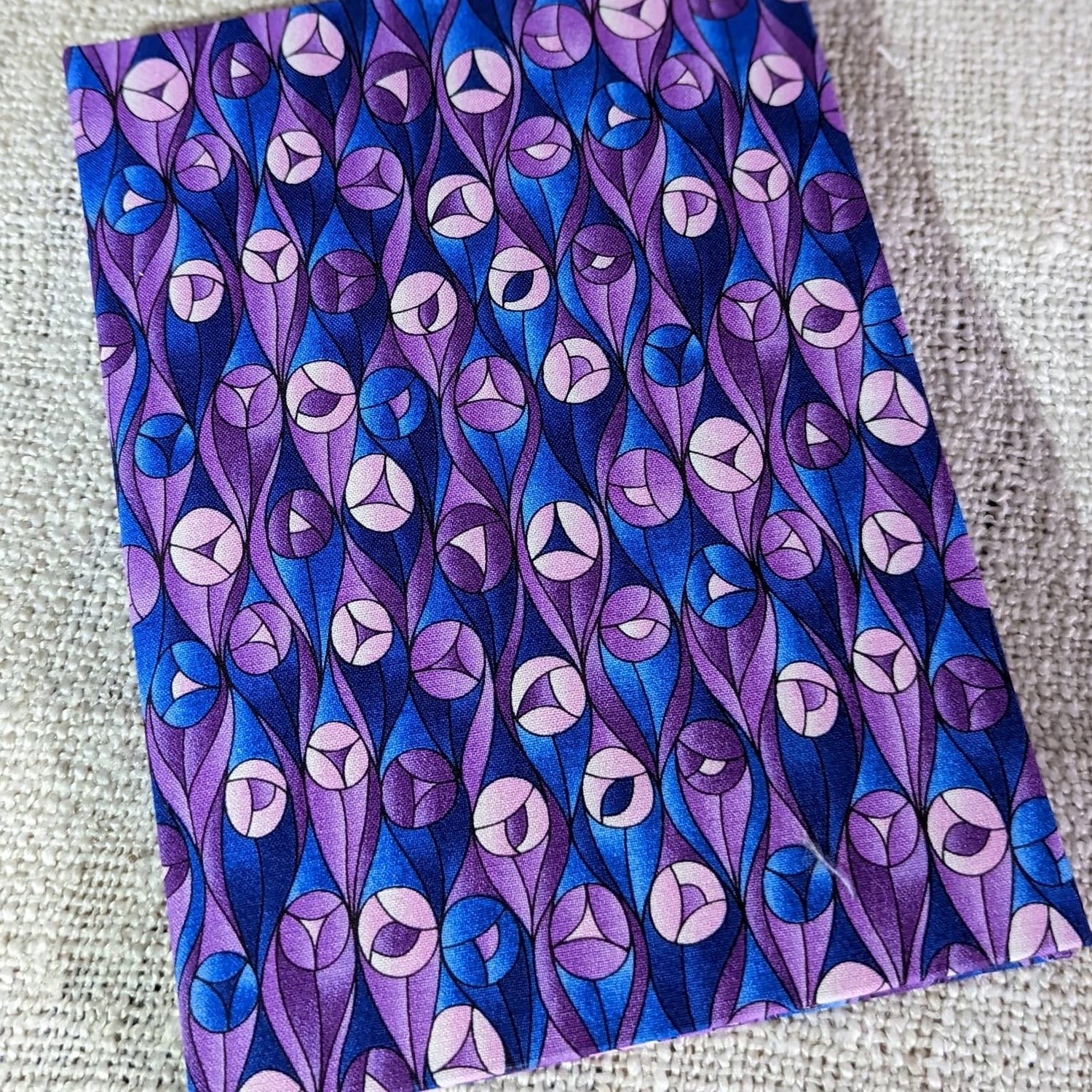 A small notebook covered with purple and blue fabric with stylised roses